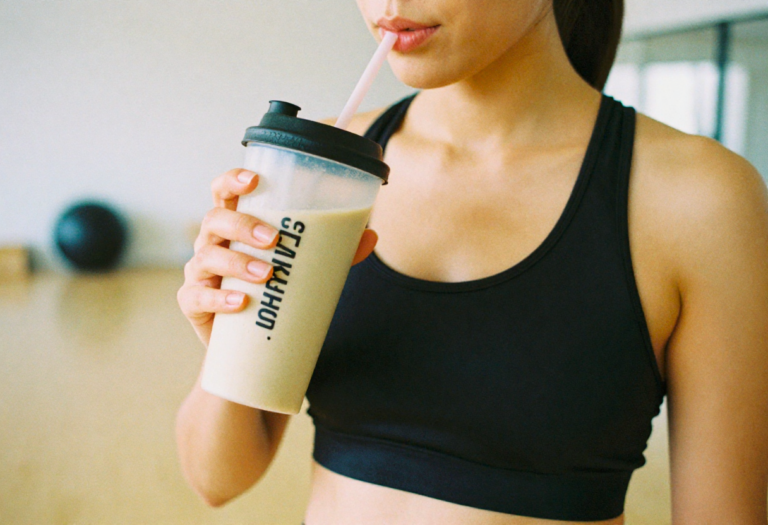Een vrouw in de sportschool die een shake vasthoudt, atletische bouw, hand met sportfles dichtbij gezicht