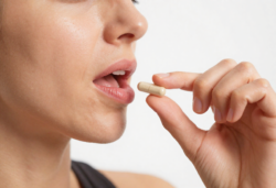 Atleet die nieuwe supplementpillen proeft, close-up van mond en handen die de capsule vasthouden, schone witte studioachtergrond, lichte transpiratie.