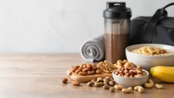 Verschillende noten voor spieropbouw naast havermout, banaan, shaker en sporttas op een houten tafel.
