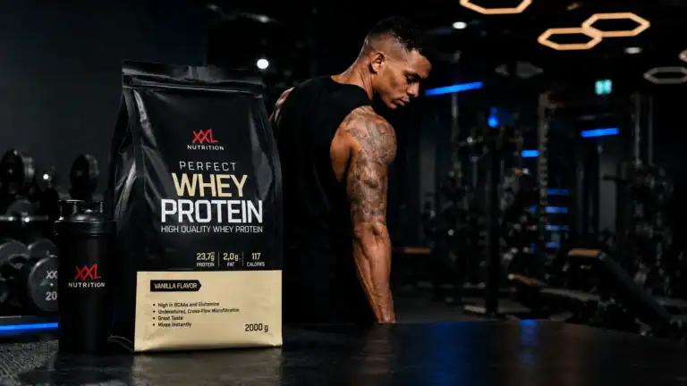 Perfect Whey Protein van XXL Nutrition met shaker op een sportschoolachtergrond.