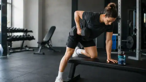Sporter traint met een dumbbell naast een pot creatine monohydraat.