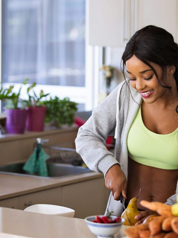 Smiling woman preparing fresh fruit in a sunlit kitchen, embodying a healthy lifestyle.