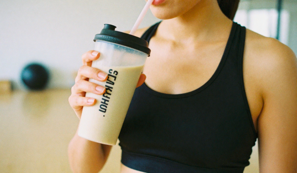 Een vrouw in de sportschool die een shake vasthoudt, atletische bouw, hand met sportfles dichtbij gezicht